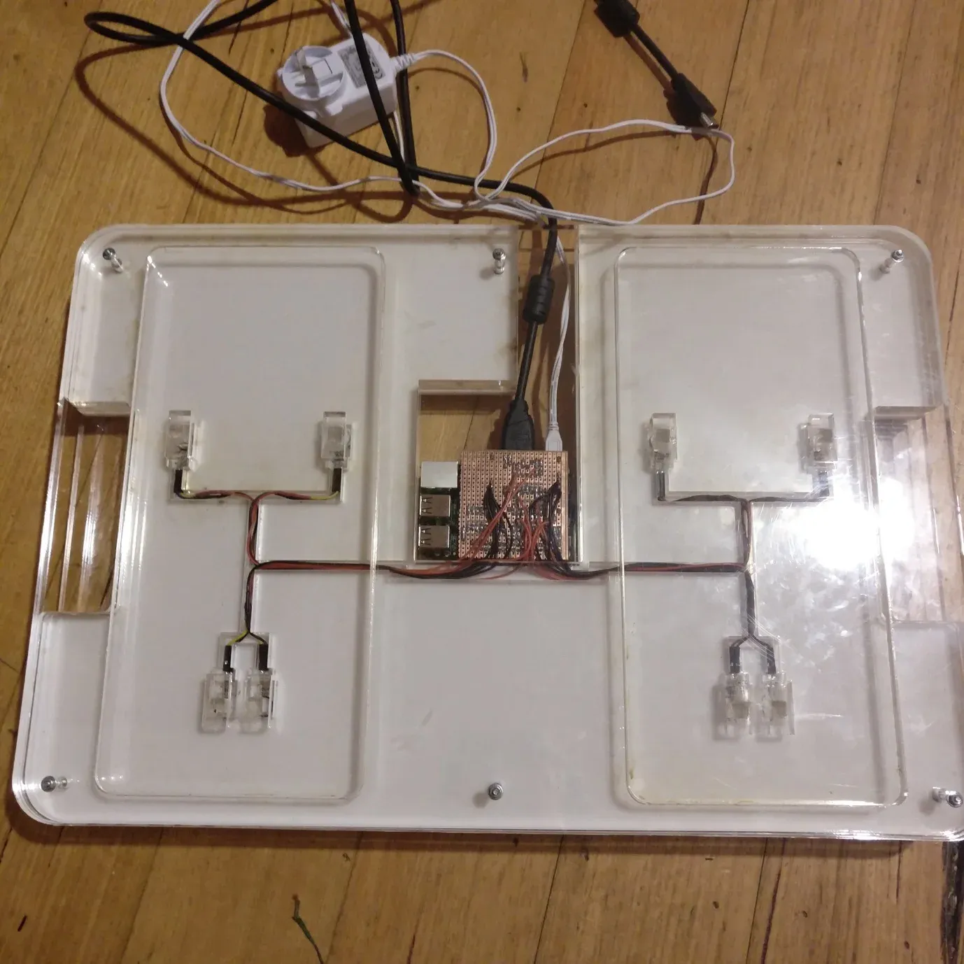The completed transparent acrylic Balance Board opened during assembly, showing two foot platforms, eight sensors, routed wiring, and central electronics.